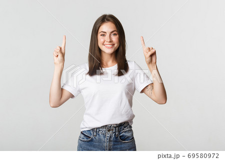Attractive smiling brunette girl pointing fingers up, showing logo 69580972