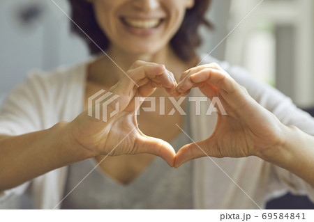 Cropped shallow focus image of happy smiling lady showing heart symbol with her hands Cropped shallow focus image of happy smiling lady showing heart symbol with her hands 69584841