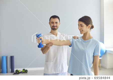 Doctor teaching young woman to do osteoporosis treatment exercise with dumbbells 69584844