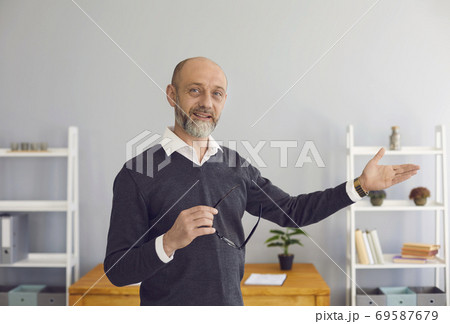 A middle-aged male professor looking at the camera uses web chat, says a business strategy remotely in a room at home. A middle-aged male professor looking at the camera uses web chat, says a business strategy remotely in a room at home. 69587679