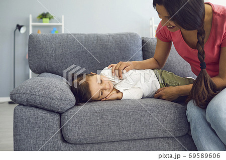 Happy young mother watching her daughter sleep on sofa in living room. Parent admiring her napping kid at home 69589606