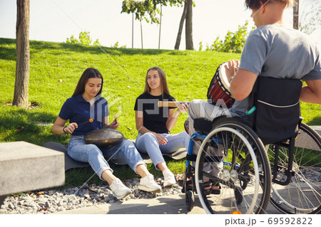 Happy handicapped man on a wheelchair spending time with friends playing live instrumental music outdoors 69592822