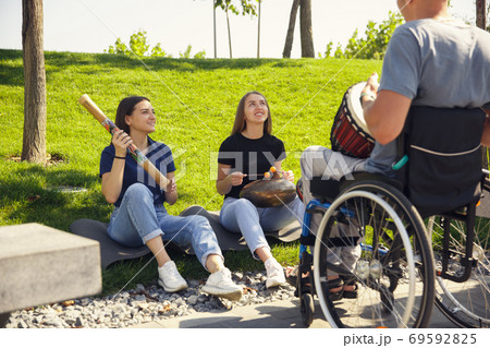 Happy handicapped man on a wheelchair spending time with friends playing live instrumental music outdoors 69592825