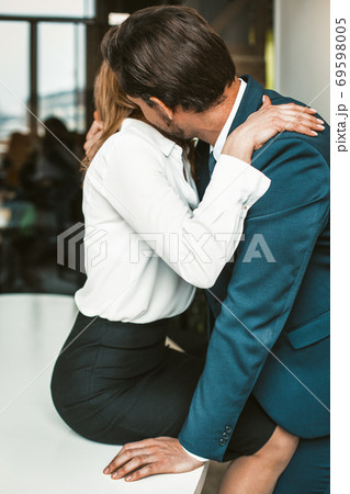 An office worker sits on a desk while a colleague kisses her neck. Passionate affair in the office workplace concept. High quality photo 69598005