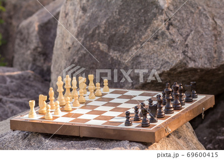Chess board with chess pieces on stone with rock on the background 69600415