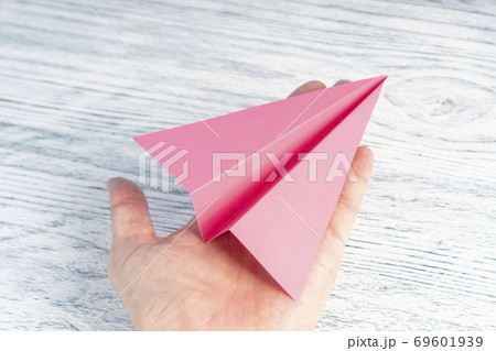 Hand of a teenager holds a pink plane on a white wooden background. Hand of a teenager holds a pink plane on a white wooden background. 69601939