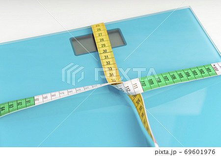 Aquamarine floor scales wrapped in a multicolored centimeter on a white background. Tied in a knot. Tools for measuring weight and body parameters when dieting Aquamarine floor scales wrapped in a multicolored centimeter on a white background. Tied in a knot. Tools for measuring weight and body parameters when dieting 69601976
