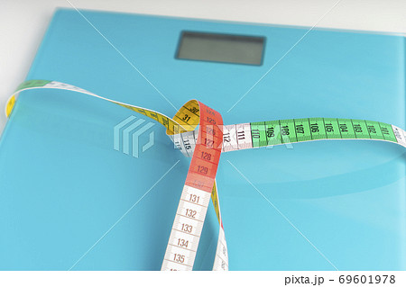 Aquamarine floor scales wrapped in a multicolored centimeter. Tied in a knot. Tools for measuring weight and body parameters when dieting Aquamarine floor scales wrapped in a multicolored centimeter. Tied in a knot. Tools for measuring weight and body parameters when dieting 69601978