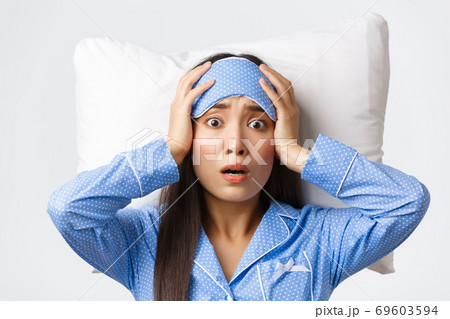 Close-up shot of panicking asian cute girl lying in bed on pillow in sleeping mask and pajamas, looking anxious and concerned, realise something bad happened, pose worried white background 69603594