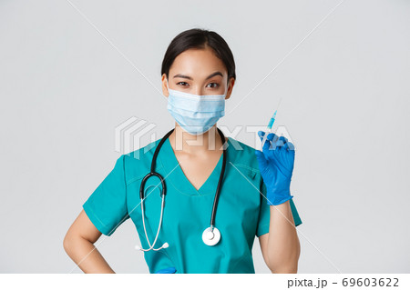 Covid-19, coronavirus disease, healthcare workers concept. Sassy cute asian female nurse, intern in medical mask and gloves holding syringe with vaccine, ready to make shot, white background Covid-19, coronavirus disease, healthcare workers concept. Sassy cute asian female nurse, intern in medical mask and gloves holding syringe with vaccine, ready to make shot, white background 69603622