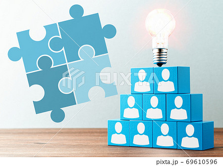 ビジネスのチームワークとソリューション。木のテーブルの上の人のアイコンが描かれた青い積木と電球。パズ 69610596