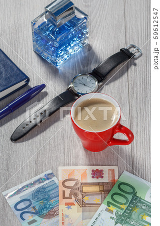 Man perfume, watch with a black leather strap, notebook, cup of coffee and euro bills 69612547