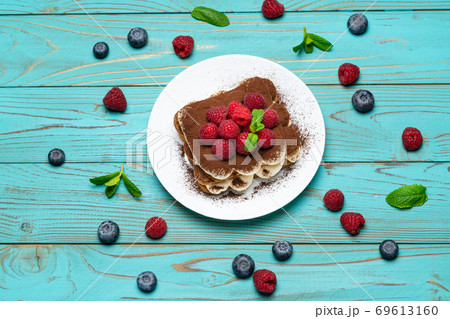 portion of Classic tiramisu dessert with raspberries and blueberries on blue wooden background 69613160
