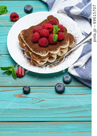 portion of Classic tiramisu dessert with raspberries and blueberries on blue wooden background portion of Classic tiramisu dessert with raspberries and blueberries on blue wooden background 69615707