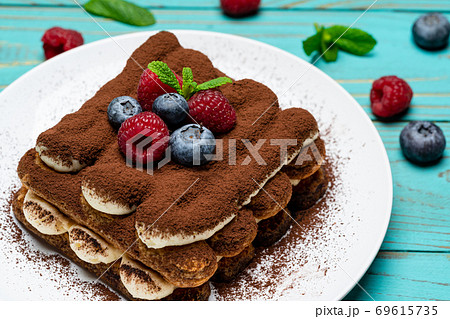portion of Classic tiramisu dessert with raspberries and blueberries on blue wooden background 69615735