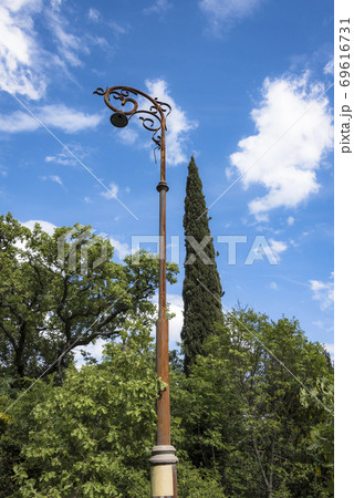 High rusty old pole with a lantern on the background of the cypress tree and cloudy sky 69616731