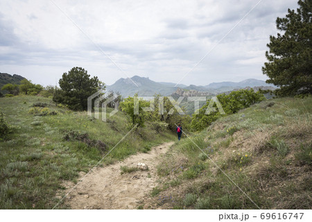 Mountain trail with the figure of a tourist on the background of the Crimean mountains in the clouds Mountain trail with the figure of a tourist on the background of the Crimean mountains in the clouds 69616747