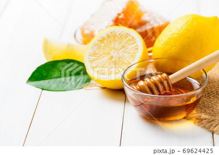 Honeycomb on dish with honey dipper with lemons on white wood background, 69624425