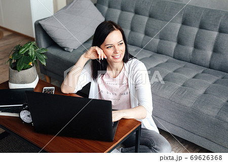 Woman student sitting on floor of her apartment with laptop and notes studying 69626368