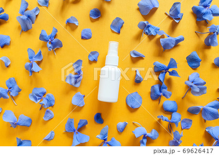 Top view and close-up of mockup  of unbranded white plastic spray bottle and petals of blue hydrangea flowers on a textured bright orange yellow background. Natural organic spa cosmetics. Flatlay. 69626417