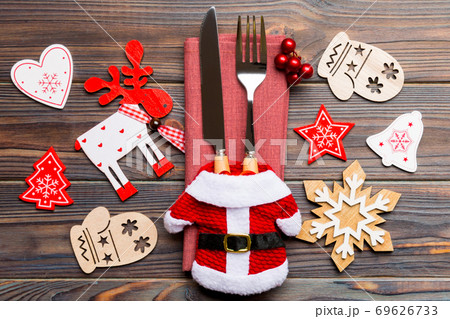 Top view of new year utensils on napkin with holiday decorations and reindeer on wooden background. Close up of christmas dinner concept Top view of new year utensils on napkin with holiday decorations and reindeer on wooden background. Close up of christmas dinner concept 69626733
