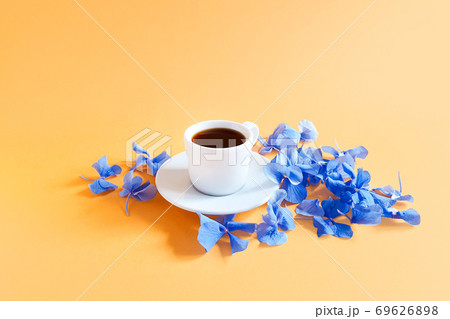 A cup of coffee and blue hydrangea flowers on a textured bright yellow-orange background. A cup of coffee and blue hydrangea flowers on a textured bright yellow-orange background. 69626898