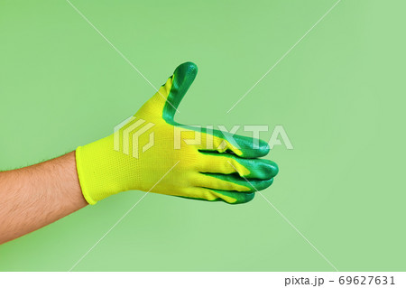 Male hand in a glove for working in the garden, vegetable garden on a green background. Open hand for handshake, showing back of the hand. 69627631