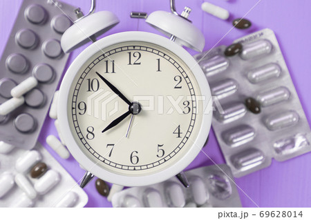 Alarm clock in a heap blister packs with medical pills on a bright neon purple background. Idea of sleep control 69628014