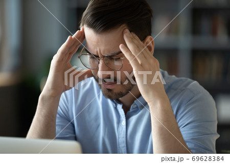 Unwell young man suffering from headache at workplace 69628384