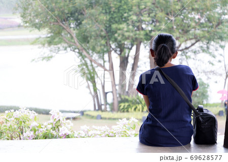 View of the back of a young woman sitting on a lookout. A lonely girl sits in nature. View of the back of a young woman sitting on a lookout. A lonely girl sits in nature. 69628577