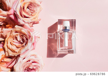 Perfume glass bottle with trendy shadow and pink golden roses on a pastel pink background. Bottle for branding and label. Luxurious flatlay. 69628786