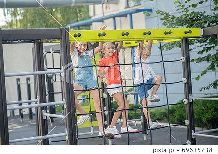 Three kids climbing on outdoor playground and looking excited 69635738