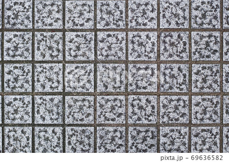 歩道舗装に敷かれた正方形の石面の凹みに溜まった汚れが模様を生み出している。 69636582