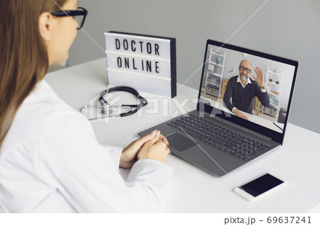 Woman doctor sitting in medical office and looking and greeting her man patient online from laptop Woman doctor sitting in medical office and looking and greeting her man patient online from laptop 69637241