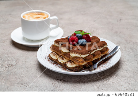 portion of Classic tiramisu dessert with raspberries, blueberries and cup of coffee on grey concrete background portion of Classic tiramisu dessert with raspberries, blueberries and cup of coffee on grey concrete background 69640531