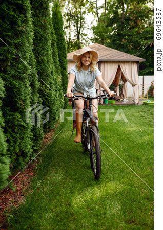 Female gardener poses on bicycle in the garden Female gardener poses on bicycle in the garden 69643537