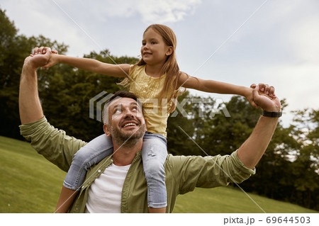 Little excited girl playing with father in park, sitting on his shoulders and smiling, they are spending great time together and having fun 69644503