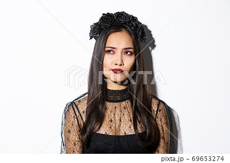 Close-up of perplexed asian woman in wicked witch costume, looking at upper left corner doubtful or indecisive, standing over white background Close-up of perplexed asian woman in wicked witch costume, looking at upper left corner doubtful or indecisive, standing over white background 69653274