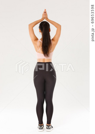 Sport, gym and healthy body concept. Full length rear view of slim brunette asian girl in active wear practice yoga, workout alone, standing with hands clasped over head in asana, meditating Sport, gym and healthy body concept. Full length rear view of slim brunette asian girl in active wear practice yoga, workout alone, standing with hands clasped over head in asana, meditating 69653598