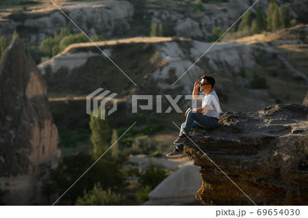 man sitting on cliff and looks into the distance. man sitting on cliff and looks into the distance. 69654030