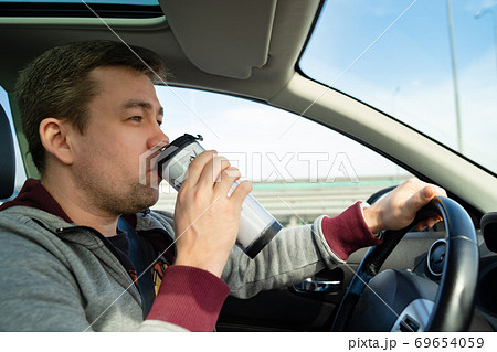 man grey sweater behind wheel of car drink coffee 69654059