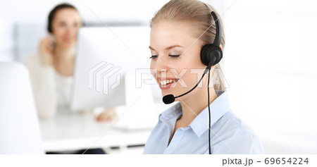 Blond woman call operator is using computer and headset for consulting clients online. Group of diverse people working as customer service occupation. Business concept Blond woman call operator is using computer and headset for consulting clients online. Group of diverse people working as customer service occupation. Business concept 69654224