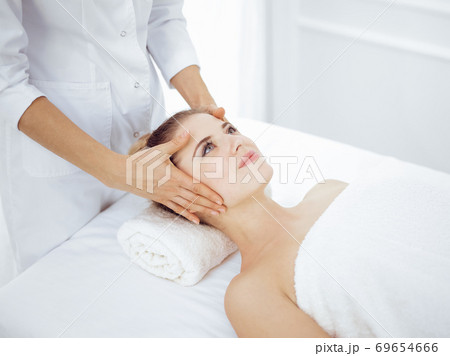 Young and blonde woman enjoying facial massage in spa salon. Beauty concept Young and blonde woman enjoying facial massage in spa salon. Beauty concept 69654666