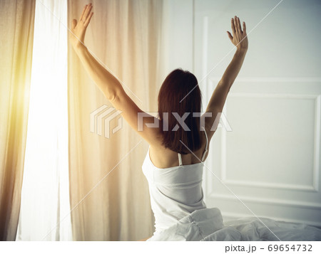 Woman stretching in bed after waking up, back view, entering a day happy and relaxed after good night sleep. Good morning and new day for brunette. Concept of Weekend, holidays 69654732