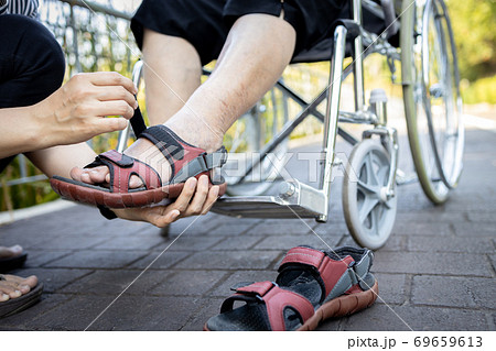 Close up of woman holding a shoes in her hand, wearing a shoes for disabled senior in a wheelchair, care,service and assistance, female caregiver helping her elderly people in outdoor at nursing home Close up of woman holding a shoes in her hand, wearing a shoes for disabled senior in a wheelchair, care,service and assistance, female caregiver helping her elderly people in outdoor at nursing home 69659613