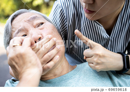 Angry asian woman covering senior mouth and showing silence gesture, keep a secret be quiet,social violence,aggression, scared elderly people with female caregiver,bad relationship,physical abuse 69659618