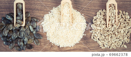 Sunflower, pumpkin and sesame seeds with wooden scoop on board, healthy nutrition concept Sunflower, pumpkin and sesame seeds with wooden scoop on board, healthy nutrition concept 69662378
