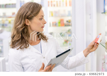 Young female pharmacist with tablet learning information about new medicaments Young female pharmacist with tablet learning information about new medicaments 69662973