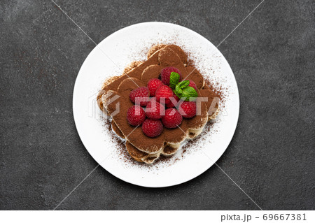 portion of Classic tiramisu dessert with raspberries on dark concrete background 69667381
