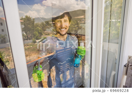 A young man cleaning the window with a window cleaner 69669228